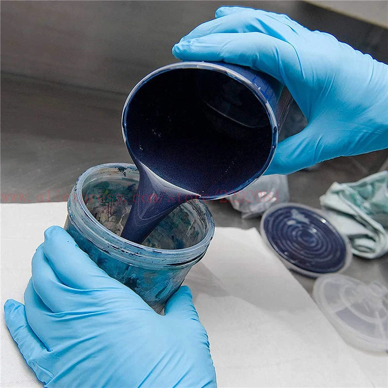 Person wearing blue gloves pouring a dark blue liquid into a container on a gray surface.