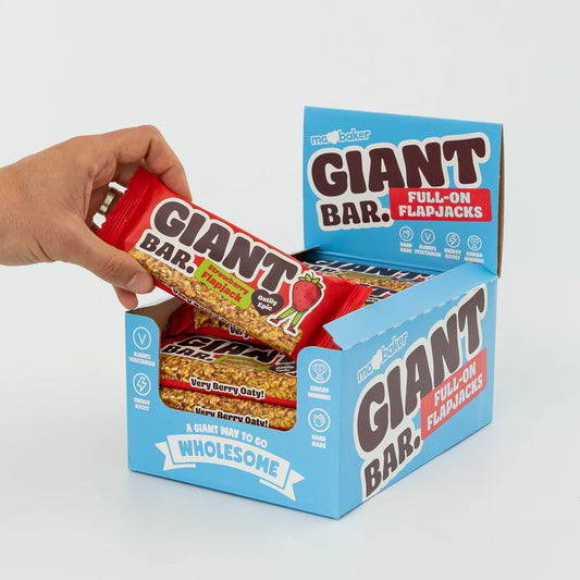 Hand holding a Giant Bar flapjack with an open box displaying multiple flavors on a light gray background.