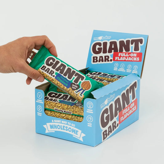 Hand reaching for a Giant Bar flapjack from an open box on a light gray background