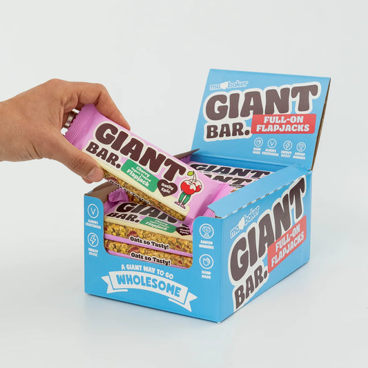 Hand holding a Giant Bar package with a display box of various flavors on a light gray background