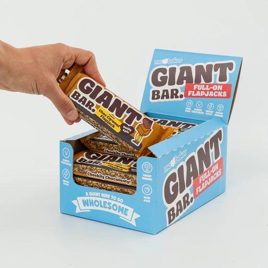 Hand holding a Giant Bar flapjack above an open box of Giant Bar flapjacks.