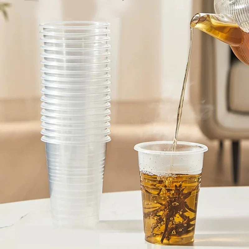 Clear plastic cups with one being filled with a yellow liquid, likely tea, on a neutral background.
