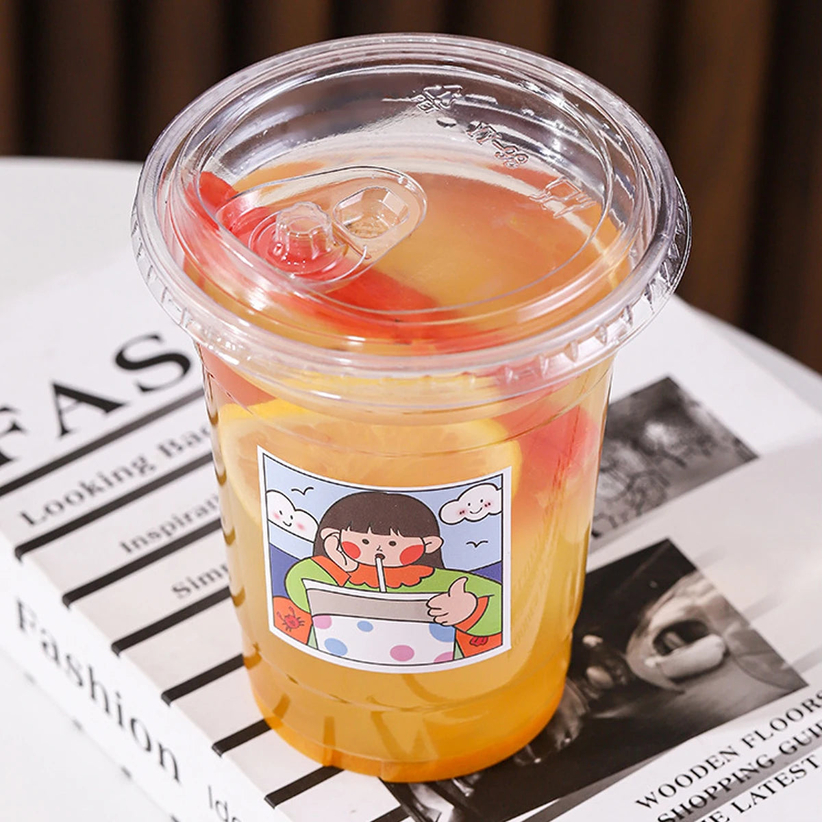 Clear plastic cup with a colorful drink and a label featuring a cartoon character on a newspaper background.