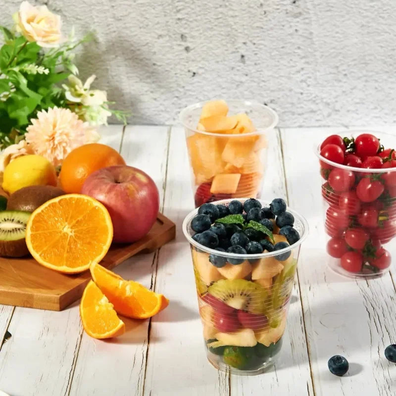 Assorted fruits including oranges, apples, kiwis, and blueberries in transparent cups on a wooden surface.