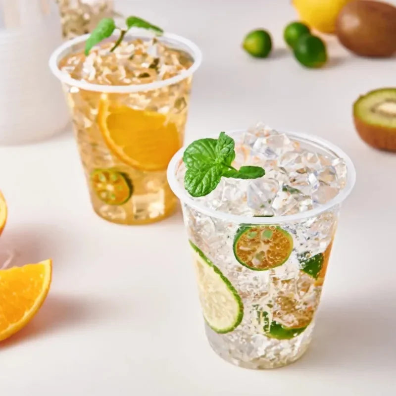 Two glasses of sparkling lemonade with fruit and mint leaves on a light surface.