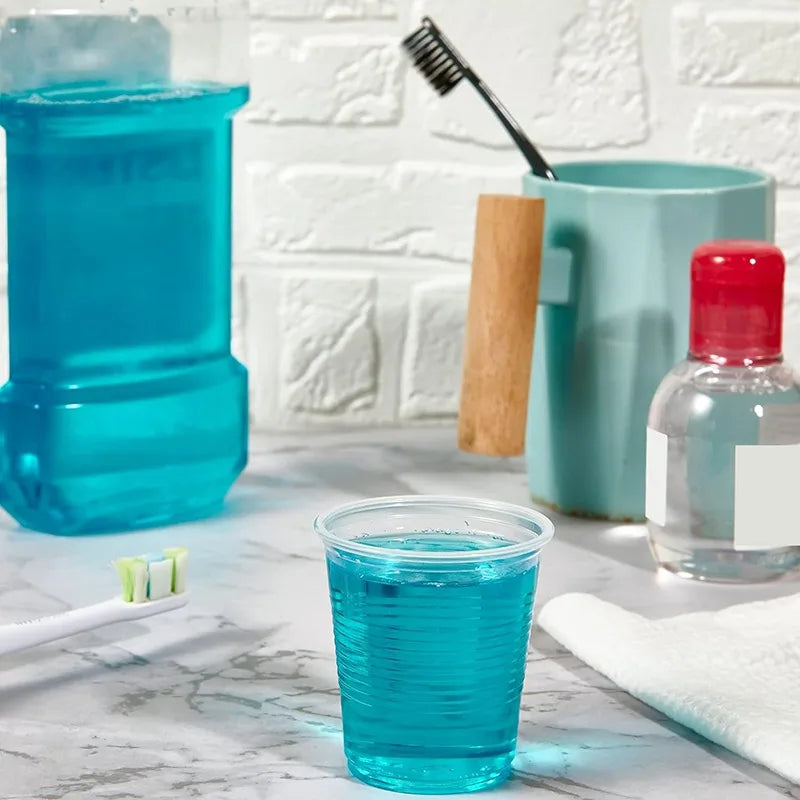 Bathroom scene with a glass of blue liquid, toothbrush, and mouthwash bottle on a marble countertop.