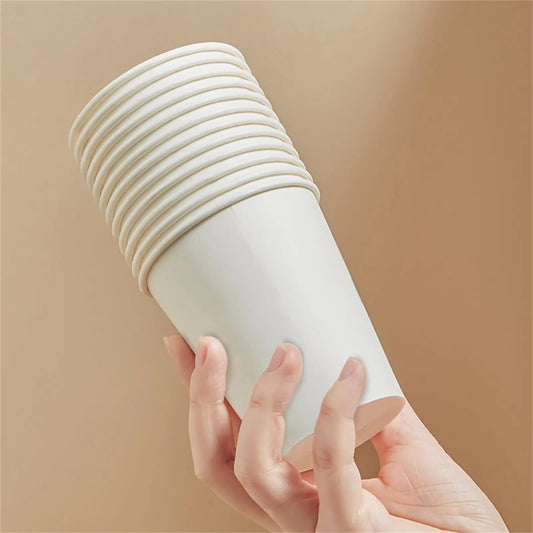 Hand holding a stack of white paper cups against a beige background