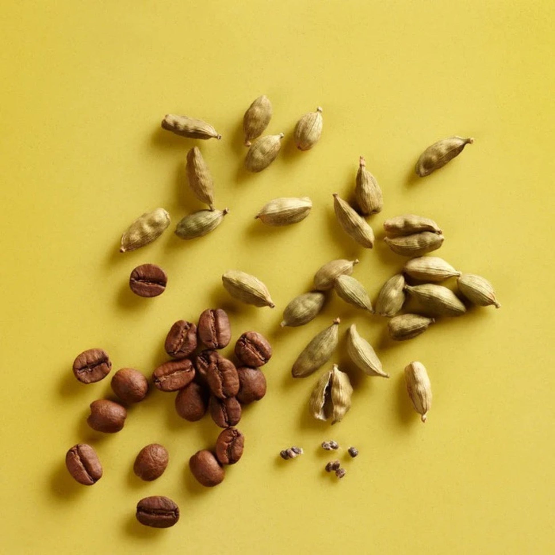 Coffee beans and cardamom pods arranged on a yellow background
