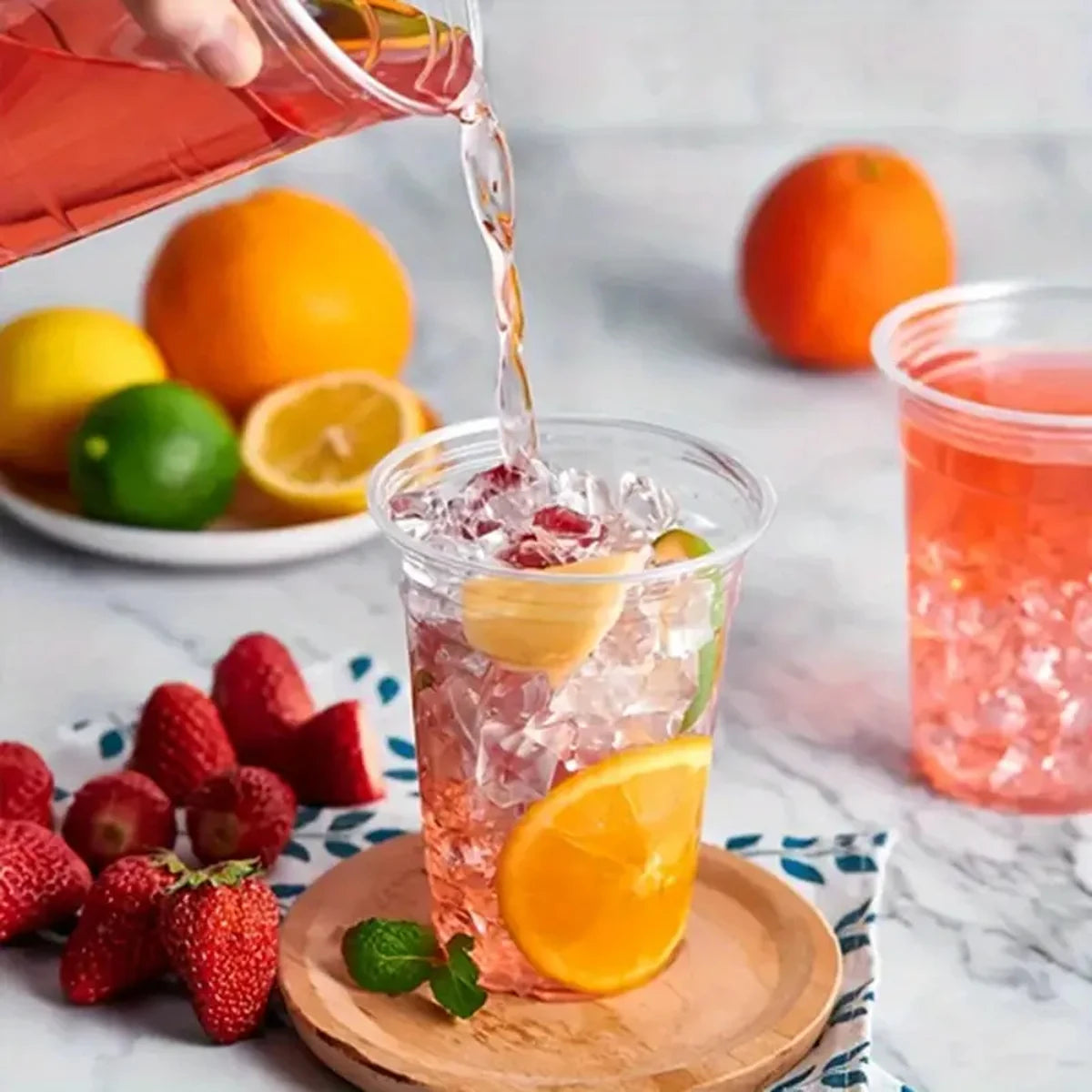 Person pouring a pink drink into a glass with fruit on a marble surface