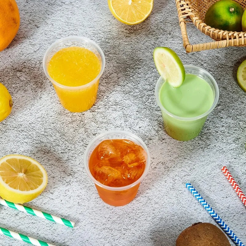 Three plastic cups with different colored drinks on a textured surface with lemons and straws.