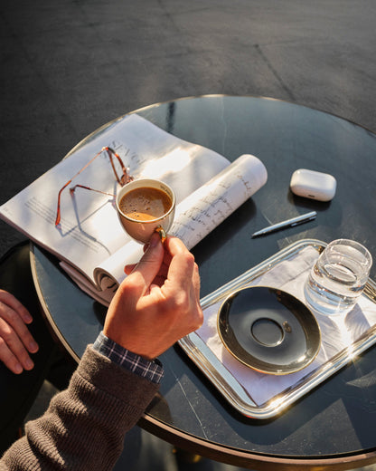 Person holding a coffee cup on a glass table with a magazine and water bottle.